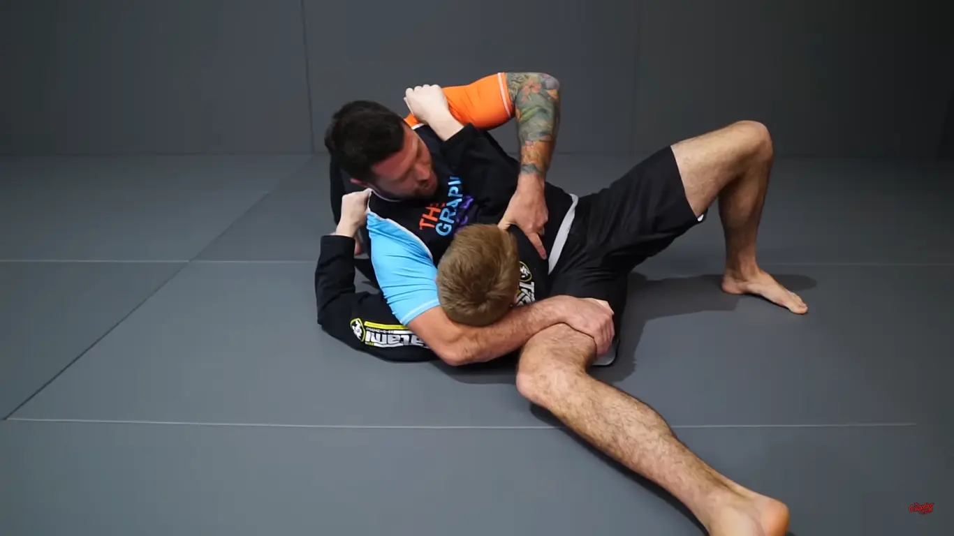 One grappler one the ground with their partner's near arm and head on their thigh. The top players near arm is wrapped around the bottom player's neck and grasping their own thigh in the scarf hold position.